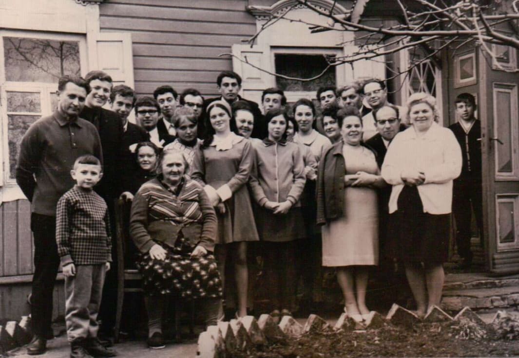 Large family and community group photo outside a house, roughly twenty people.