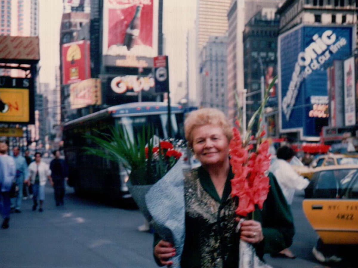 Masha holding red gladioli in Times Square, New York, smiling broadly.