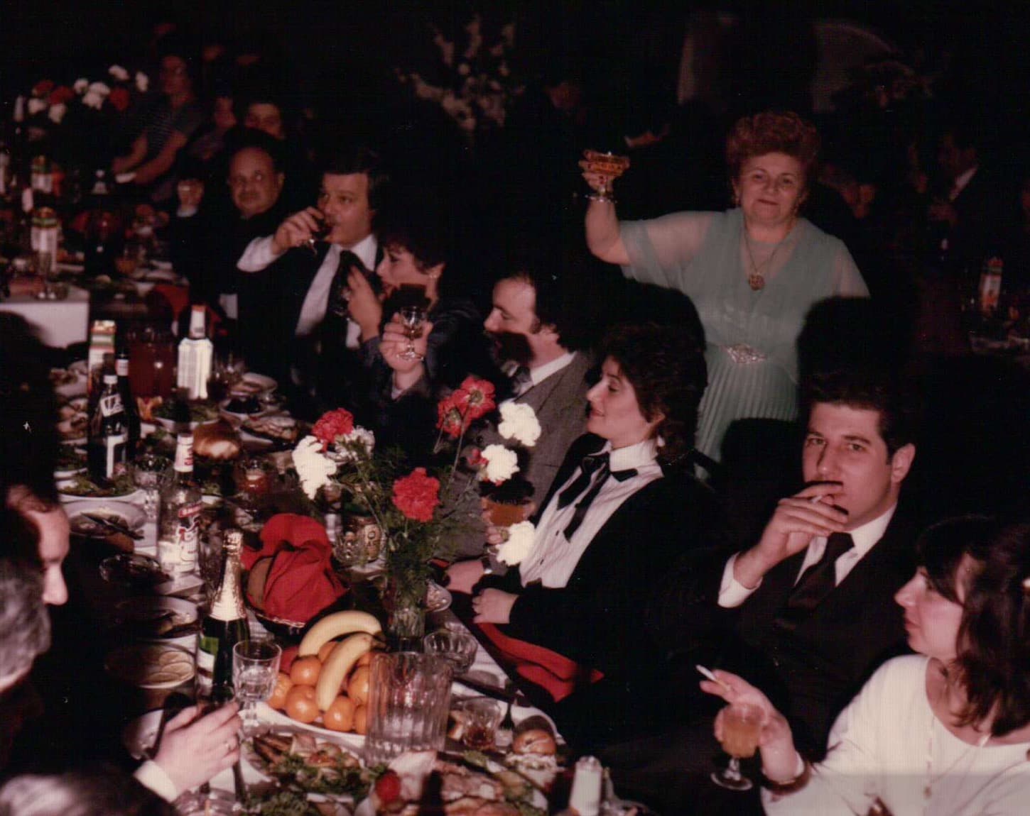 Masha raising a toast at a wedding celebration, large table with flowers.